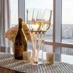 wine glasses and bottles on a table in front of a window with the city skyline outside