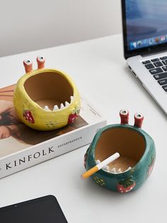 a desk with a book, cup holder and laptop on it next to a toy toothbrush holder