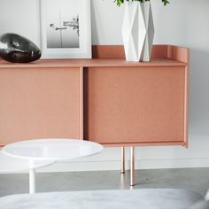 a white vase with flowers on top of a pink cabinet