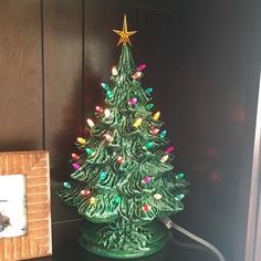 a small green christmas tree sitting on top of a table next to a framed photo