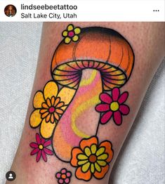 a colorful mushroom tattoo with flowers on the side of her leg and an inscription underneath it