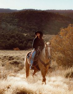 a woman riding on the back of a brown horse through a dry grass covered field