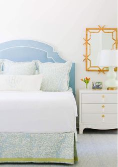 a white bed sitting next to a blue headboard and a mirror on the wall