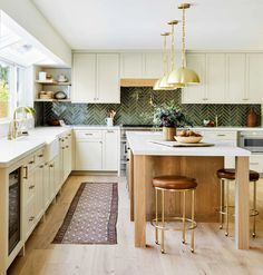 a kitchen with white cabinets and wooden floors, gold pendant lights over the island counter