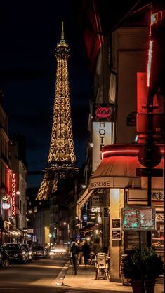 the eiffel tower lit up at night with people walking on the sidewalk below