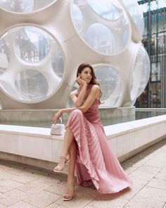 a woman in a pink dress sitting on a ledge