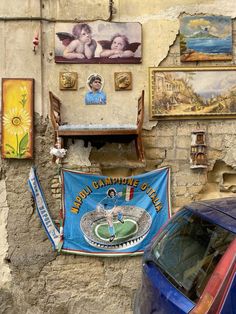 a blue car parked in front of a wall with paintings on it