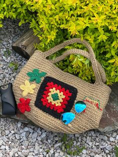 a crocheted purse sitting on top of a stone ground next to green bushes