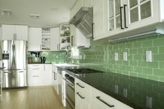 a kitchen with white cabinets and green tile backsplash, stainless steel appliances and wood flooring