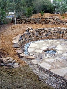 a stone fire pit surrounded by dry grass and rocks, with trees in the background