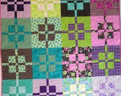 a colorful quilt with squares and flowers on the front, in shades of blue, green, purple, and pink