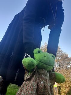 a green stuffed animal sitting on top of a person's leg in the grass