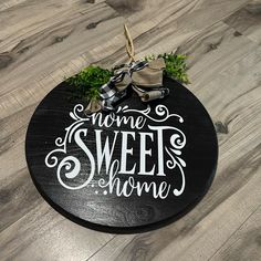 a round wooden sign that says home sweet home on top of a wood floor with a bow