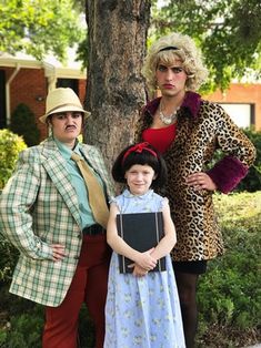 two adults and a child standing in front of a tree