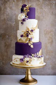 a three tiered cake with purple and white flowers on the top is sitting on a gold plate