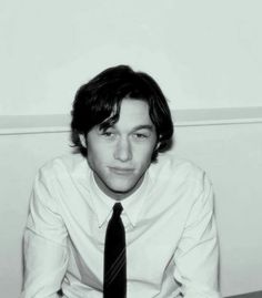 black and white photograph of a young man wearing a shirt and tie sitting on the floor