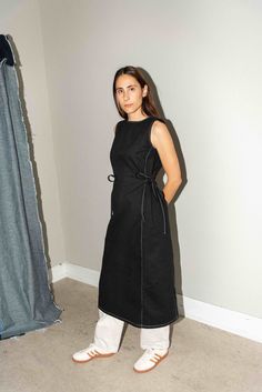 a woman is standing in front of a curtain wearing white shoes and a black dress