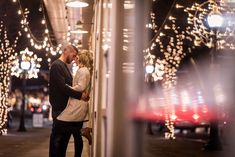 a man and woman standing next to each other in front of lights on the street