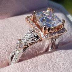 an engagement ring with a princess cut diamond surrounded by smaller round diamonds on a white cloth