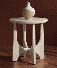 a white vase sitting on top of a table next to a red wall and wooden floor