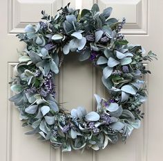 a wreath is hanging on the front door with purple flowers and greenery around it