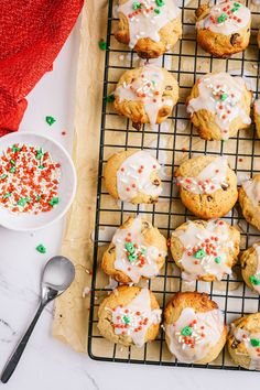 cookies with white icing and sprinkles on a cooling rack next to a bowl of candy