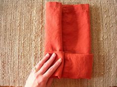 someone is holding an orange napkin on top of a brown carpeted area with a hand