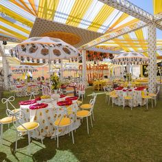 an outdoor dining area with yellow and white chairs, tables and umbrellas on grass