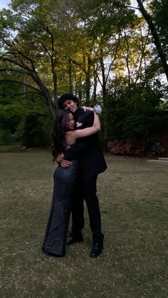 a man and woman hugging in the middle of a grassy area with trees behind them