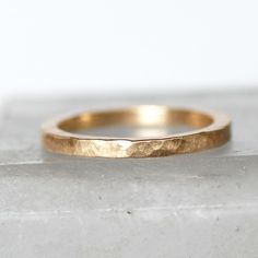 a gold wedding band sitting on top of a marble slab with the edge of it