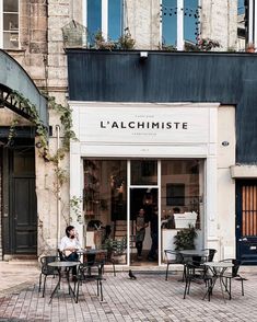 two people sitting at tables in front of a store with plants growing on the windows