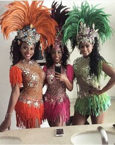 three women dressed in colorful costumes standing next to each other near a sink and mirror