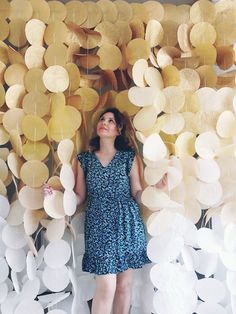 a woman standing in front of a wall made out of paper circles and leaves with her eyes closed