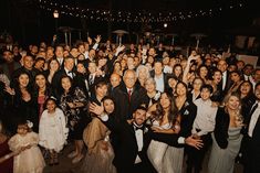 a large group of people posing for a photo at a wedding or other event with their arms in the air