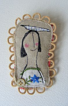 an embroidered brooch with a woman's face and flowers on the side, sitting on a white surface