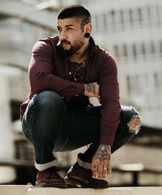 a man sitting on top of a cement wall with his hands crossed and looking at the camera