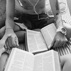 two people sitting on a bed with an open book in their hands and earphones attached to them