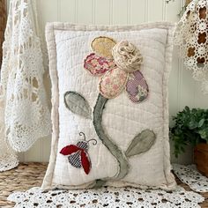 a decorative pillow with flowers on it sitting on a lace doily next to a potted plant