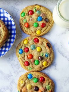 three cookies with m & m candy on them and a glass of milk next to it