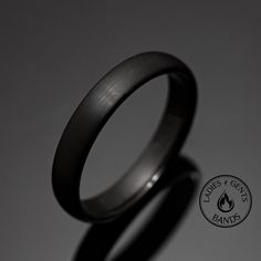 a black wedding band with a flame logo on the front and back side, against a gray background