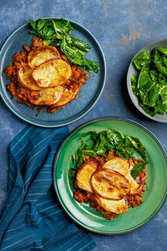 two plates filled with food on top of a blue tablecloth next to green vegetables