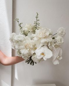 a bouquet of white flowers is held up against a wall by someone's hand