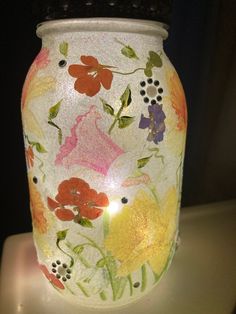 a vase with flowers painted on it is sitting on a white surface and lit by a candle