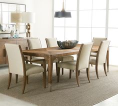 a dining room table with chairs and a bowl on it's centerpiece in front of a large window