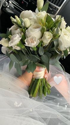 a bouquet of white roses in someone's hand on the dashboard of a car