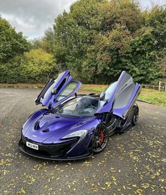 two blue sports cars parked next to each other in a parking lot with trees behind them