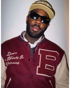 a man with sunglasses and a hat on posing for a photo in front of a white wall