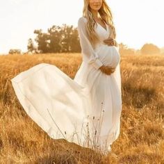 a pregnant woman in a white dress standing in a field