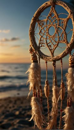 a dream catcher sitting on top of a sandy beach next to the ocean at sunset