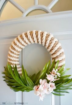 a diy coastal wreath with flowers and rope hanging on the front door for an easy summer decor idea